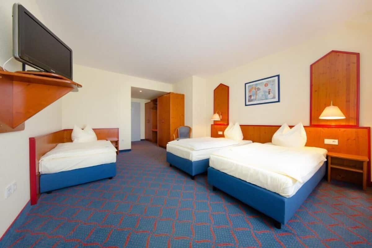 Ein Hotelzimmer mit zwei Einzelbetten, einem Fernseher auf einem Tisch, einem Schreibtisch und einem Spiegel.