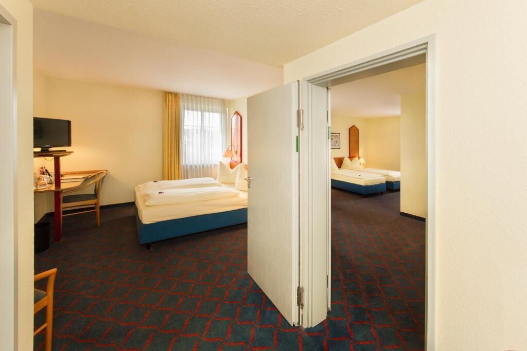 Habitación de hotel con cama, escritorio y televisión, además de un espejo.