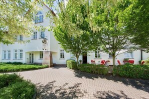 A white building with a paved entrance, surrounded by greenery and red chairs. - Montana Hotel Kassel-Süd (Guxhagen)