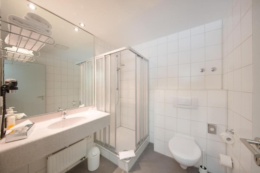 A modern bathroom with a glass shower enclosure, a sink with toiletries, and a toilet.
