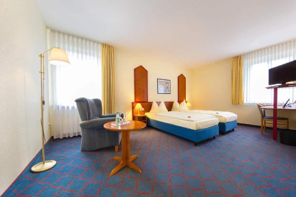 Ein Hotelzimmer mit Bett, Schreibtisch, Stuhl, Stehlampe und einem kleinen Tisch.
