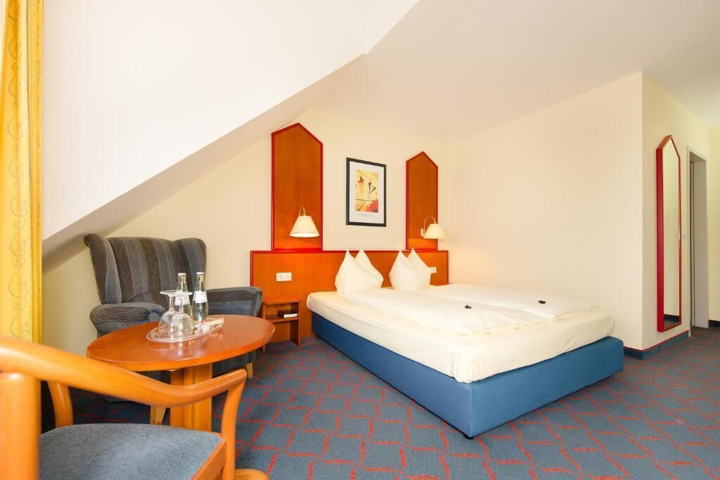 A hotel room with a bed, a desk, a chair, and a small table.