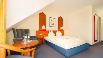 A hotel room with a bed, a desk, a chair, and a small table.