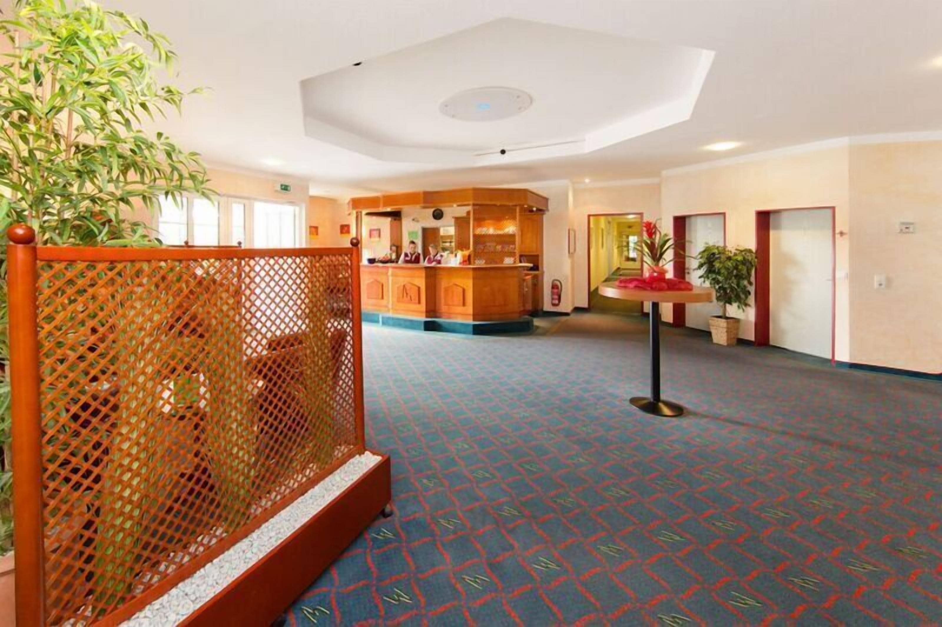 A hotel lobby with a reception desk, a decorative plant, and a patterned carpet.