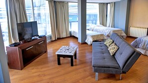 Ein modernes Hotelzimmer mit einem großen Bett, einer Couch, einem Fernseher auf einer Holzkonsole und einem kleinen Tisch.