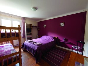 A bedroom with a wooden bed, purple walls, a window, a wardrobe, and a desk with a lamp.