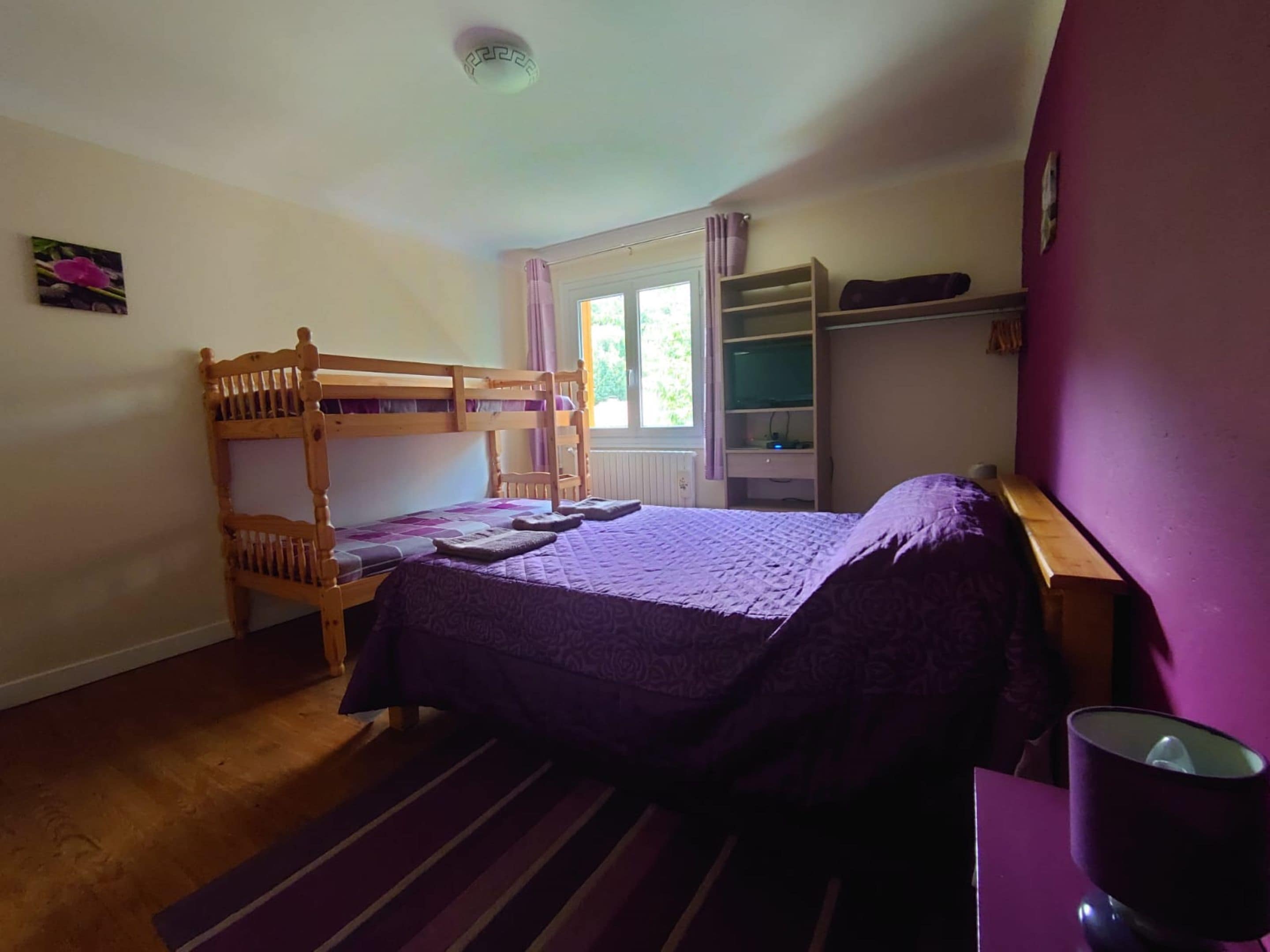 A bedroom with a bunk bed, a desk, a chair, a window with curtains, and a shelf with books.