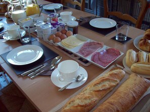 A breakfast table with plates of eggs, ham, and bread, along with cups and a pitcher of juice.