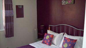 Quarto com cama, roupa de cama roxa e almofadas coloridas.