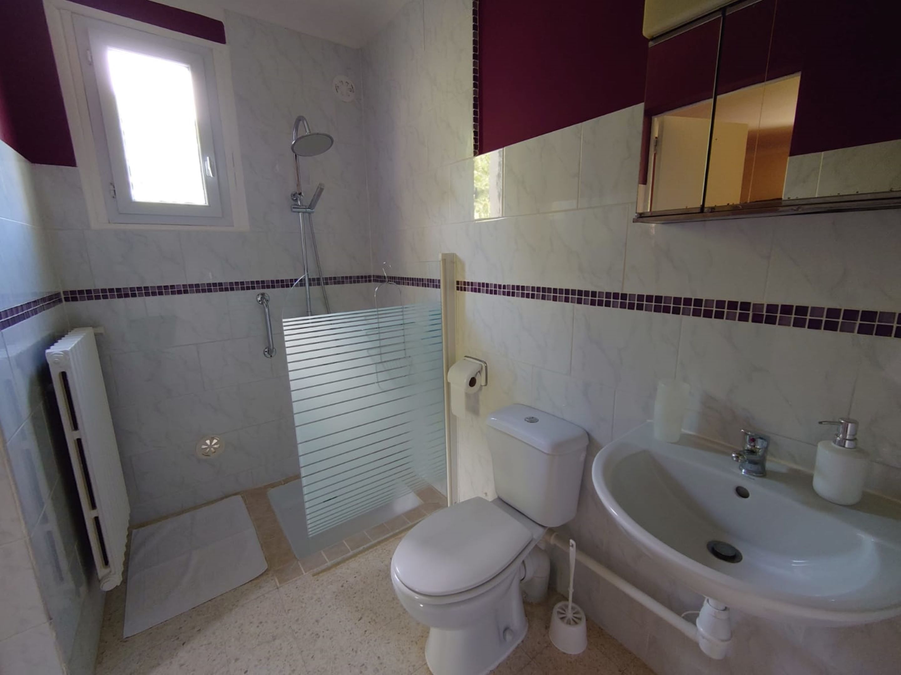 A bathroom with a shower, toilet, sink, and a window.