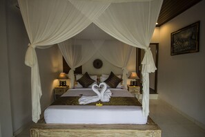 Una cama con dosel y cuatro columnas, con una decoración de toalla con forma de cisne, dos mesitas de noche con lámparas y un cuadro en la pared.