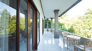 A balcony with a view of lush greenery, a wooden table and chairs, and a stone column. - Akusara Guest House (Ubud)