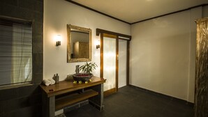 A modern bathroom with a wooden vanity, a large mirror, and a stone wall. - Akusara Guest House (Ubud)