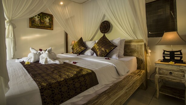 A bed with white linens, a decorative headboard, and a bedside table with a lamp. - Akusara Guest House (Ubud)