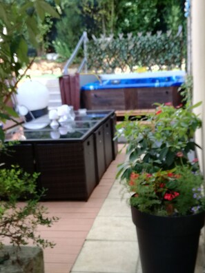 A patio area with a hot tub, a wooden deck, and a potted plant with red flowers. - Cluny clos fleury (Cluny)