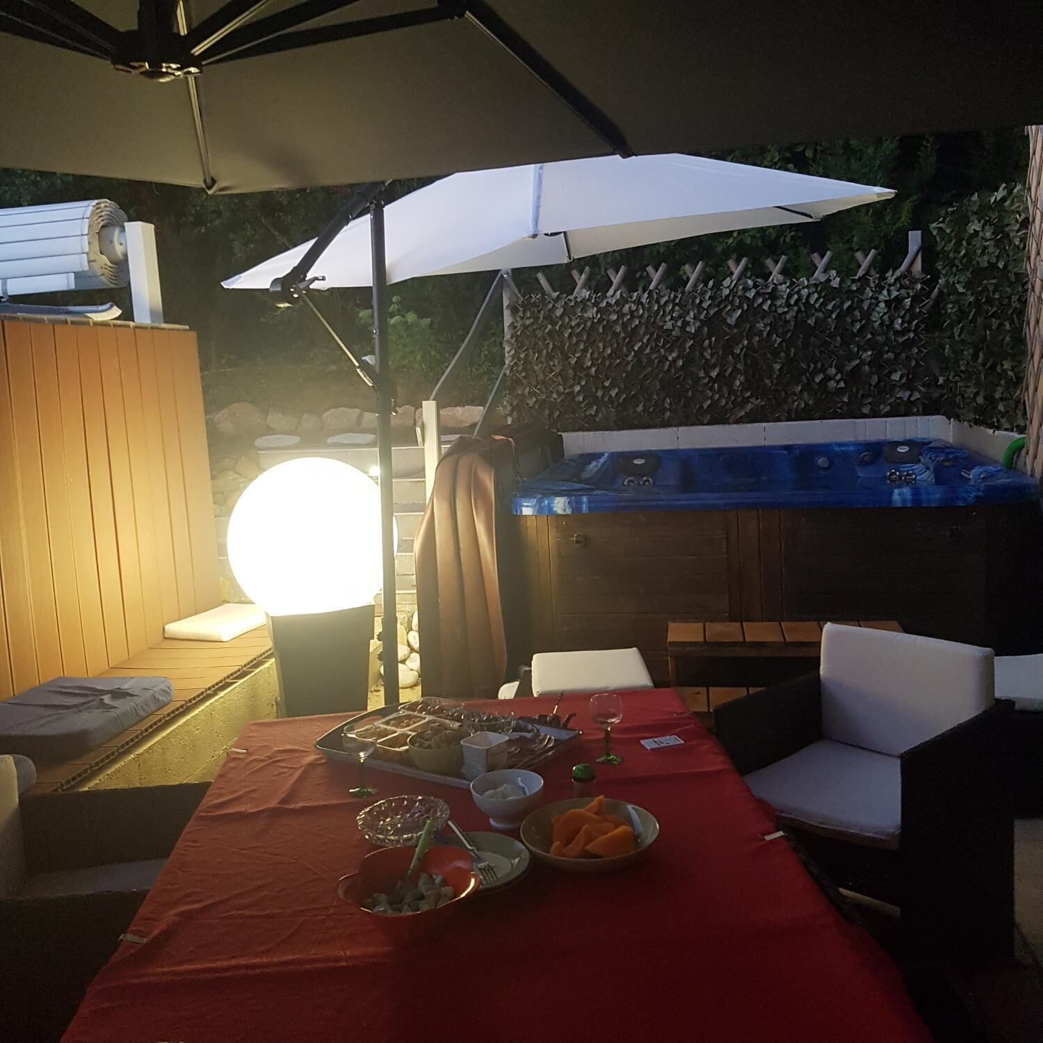 Een terras met een eettafel voor twee personen, een jacuzzi en een houten terras.