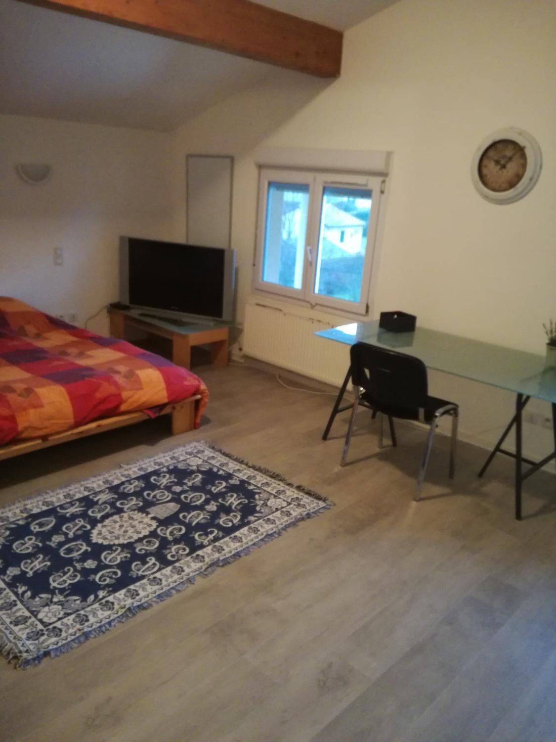 Ein Schlafzimmer mit einem Bett, einem Fernseher, einem Schreibtisch mit Stuhl und einem Fenster.