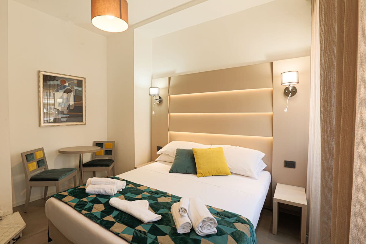Une chambre d’hôtel avec un lit, deux chaises, une petite table et un tableau au mur.