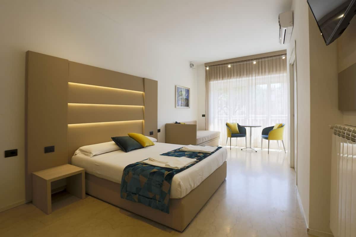 Une chambre d’hôtel moderne avec un grand lit, une table de chevet et un petit coin salon avec deux fauteuils.