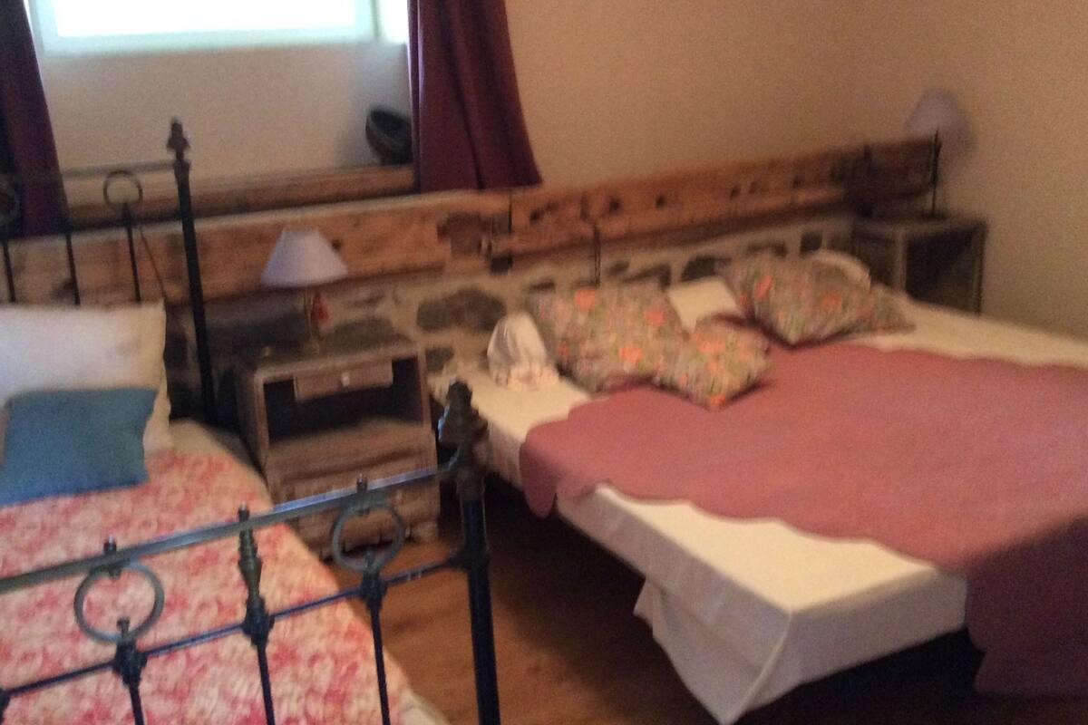 A bedroom with a wooden headboard, a bed with a white sheet and floral pillow, a bedside table with a lamp, and a window with curtains.