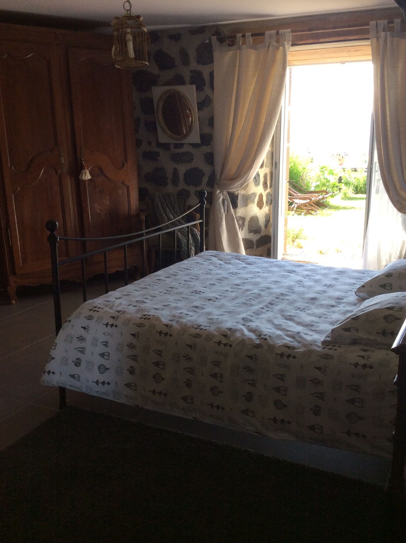 Ein Schlafzimmer mit Bett, Holzschrank, Steinwand und einem Fenster mit Vorhängen.