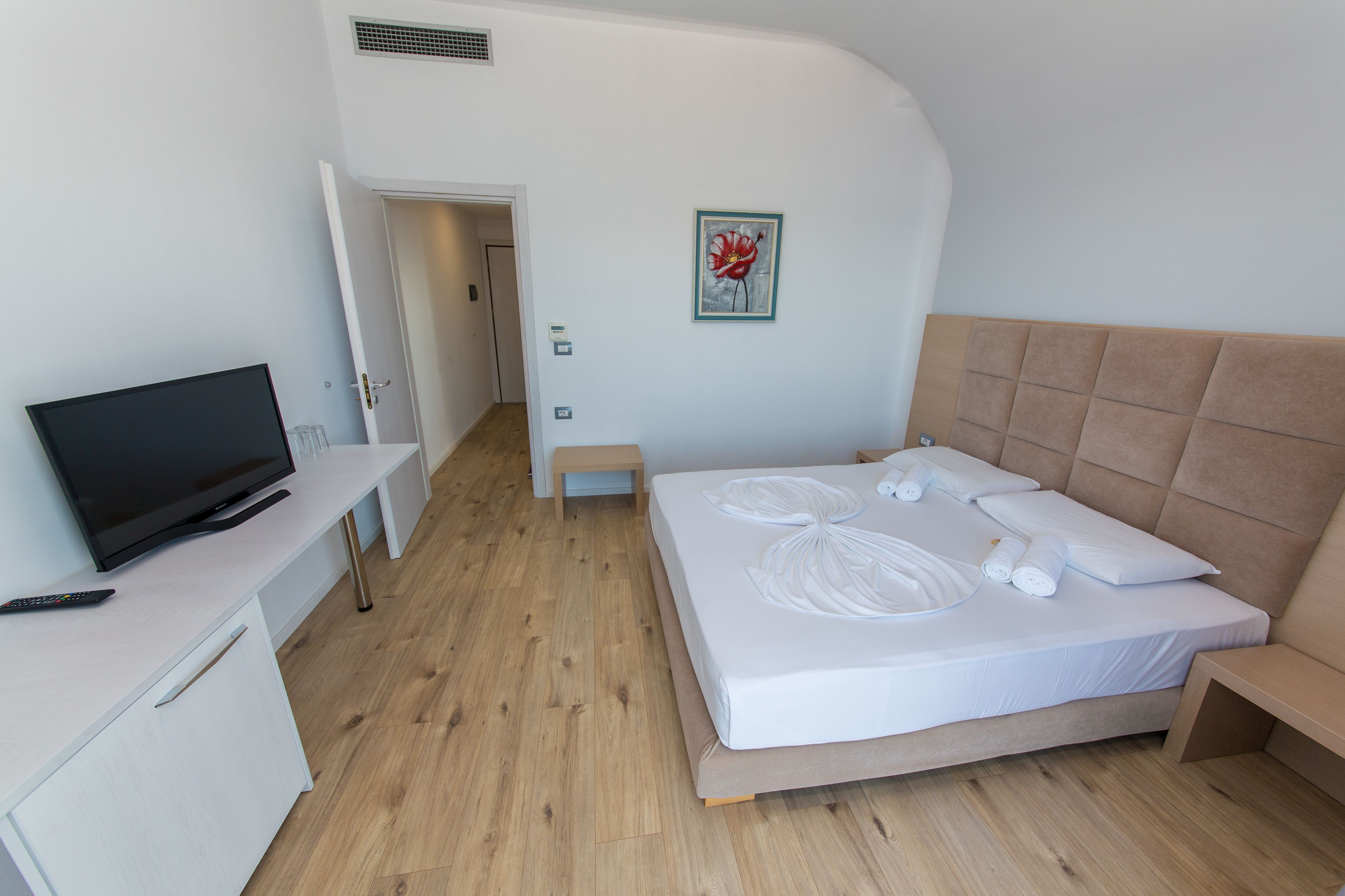 Ein modernes Hotelzimmer mit einem Bett, einem Fernseher, einem Schreibtisch und einer Tür zu einem anderen Raum.