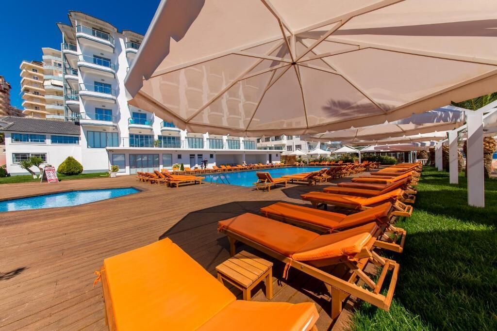 A poolside area with sun loungers and umbrellas, a pool, and a modern building in the background.