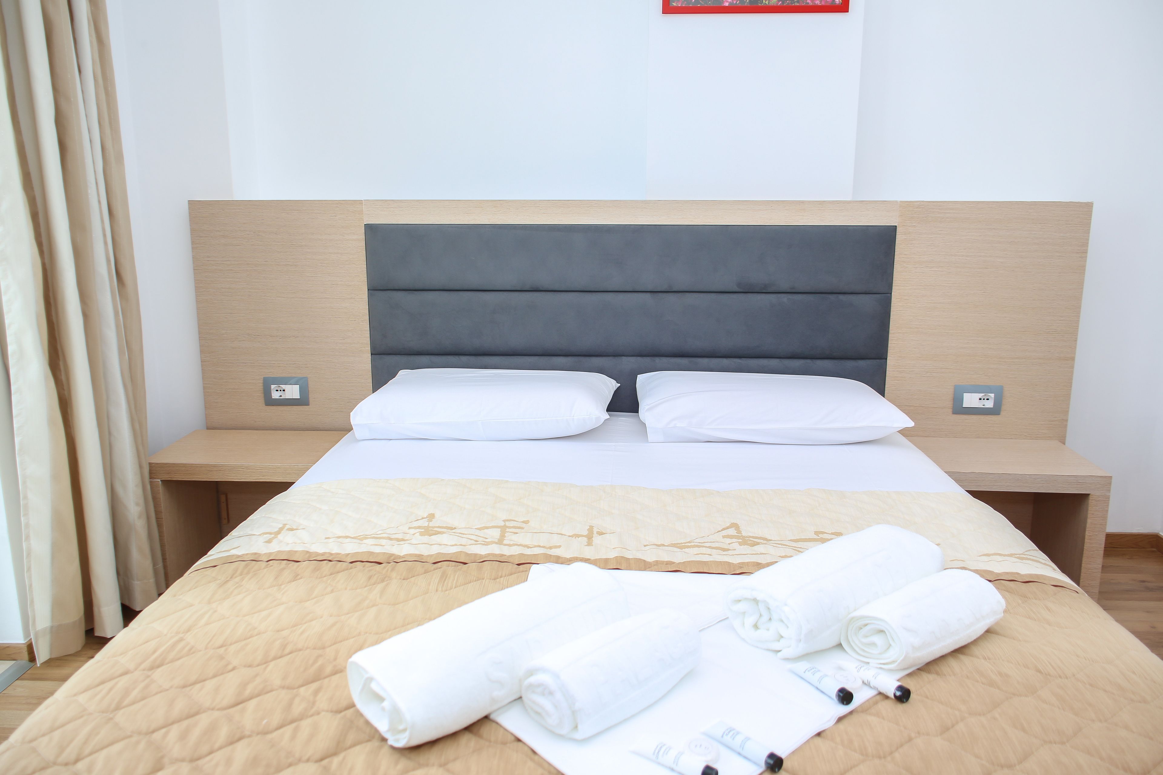 A hotel room with a bed, two bedside tables, and a wooden headboard.