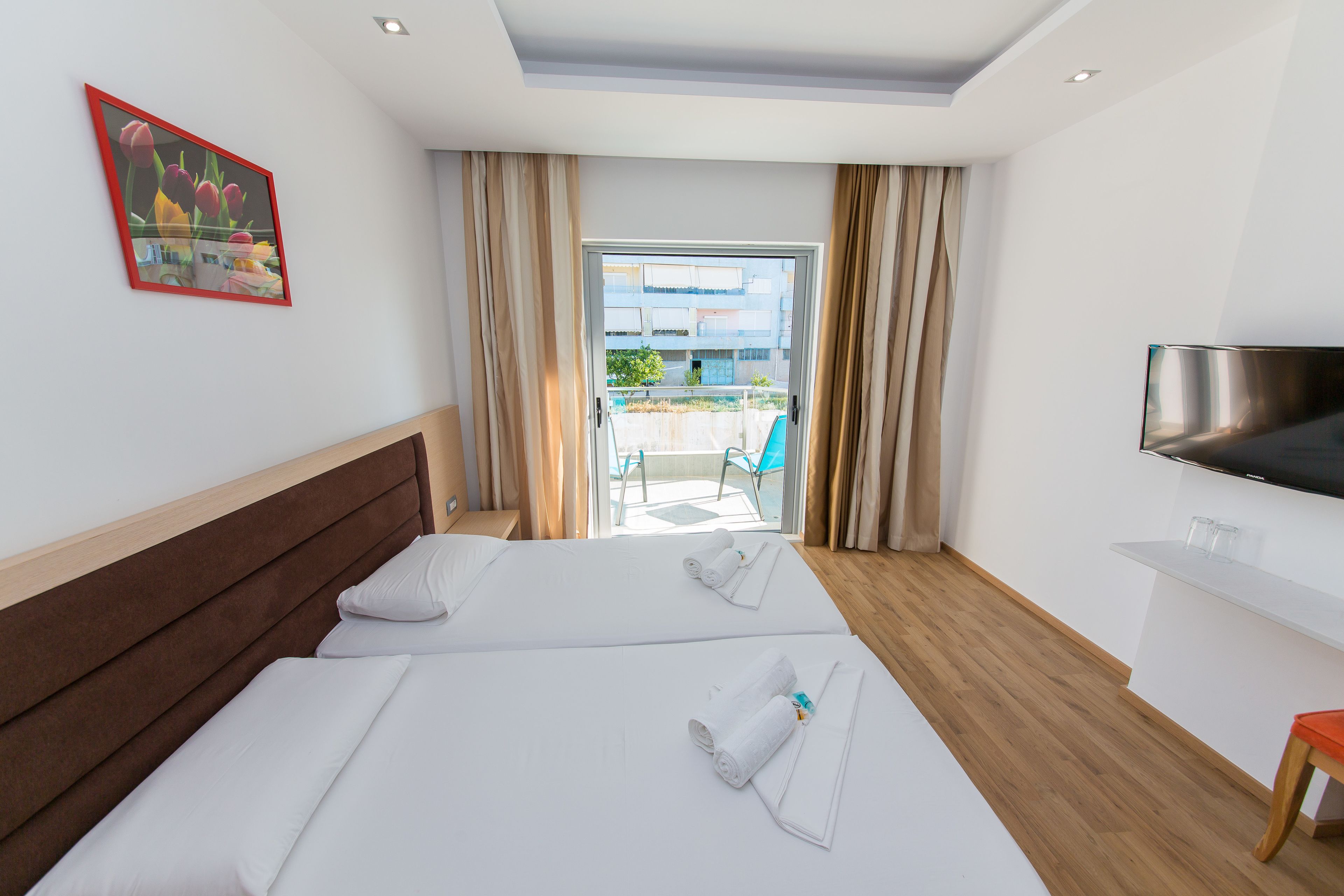 A hotel room with two beds, a TV, and a balcony with a view of the outside.