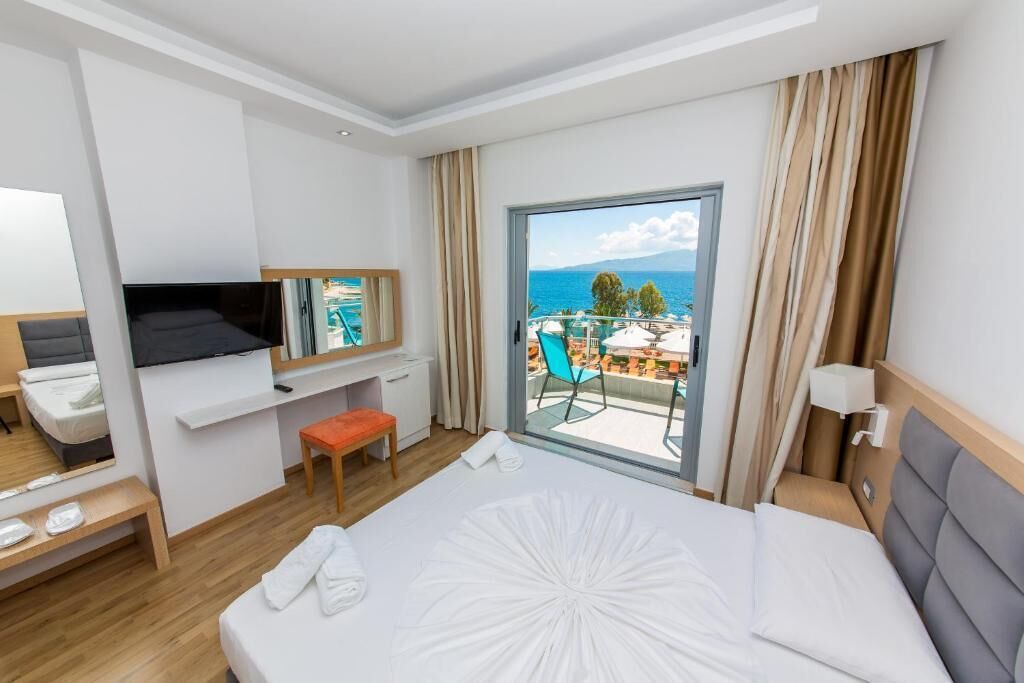 A hotel room with a bed, a TV, a desk, a chair, and a balcony with a view of the sea.