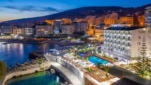 Un hotel frente al mar con piscina, varios balcones y vistas tanto al océano como a la ciudad.