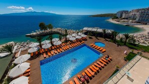 Zona de piscina en un resort, con vistas al mar, sillas de descanso, sombrillas y una piscina.