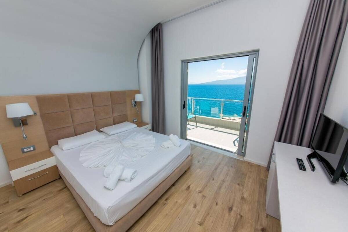 A hotel room with a bed, a desk, a TV, and a balcony with a view of the sea.