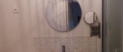 Un baño con lavamanos blanco, un espejo redondo y zona de ducha.