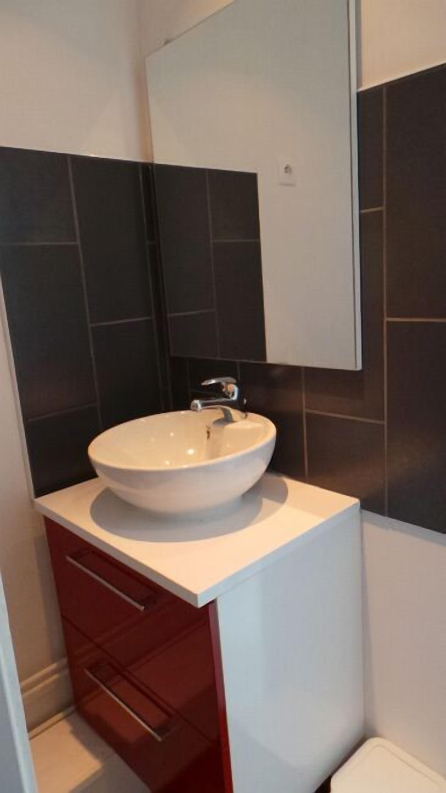 A bathroom with a white sink, dark tiles, and a red cabinet.