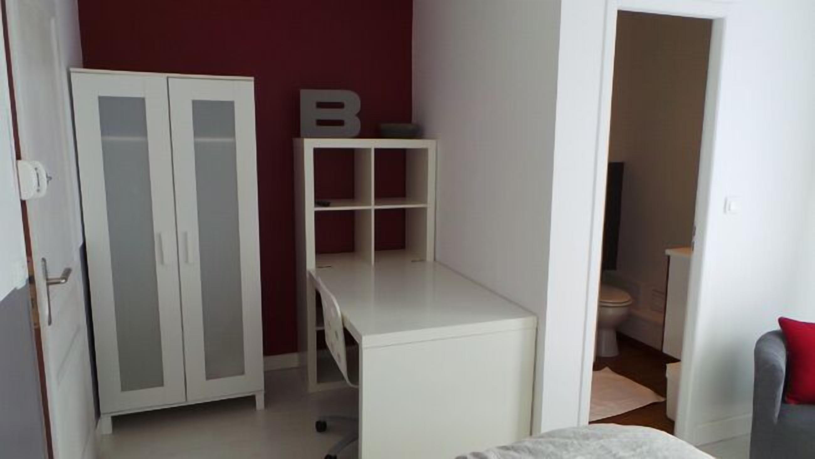 Una habitación con un armario blanco, un escritorio y una pared decorada en rojo.