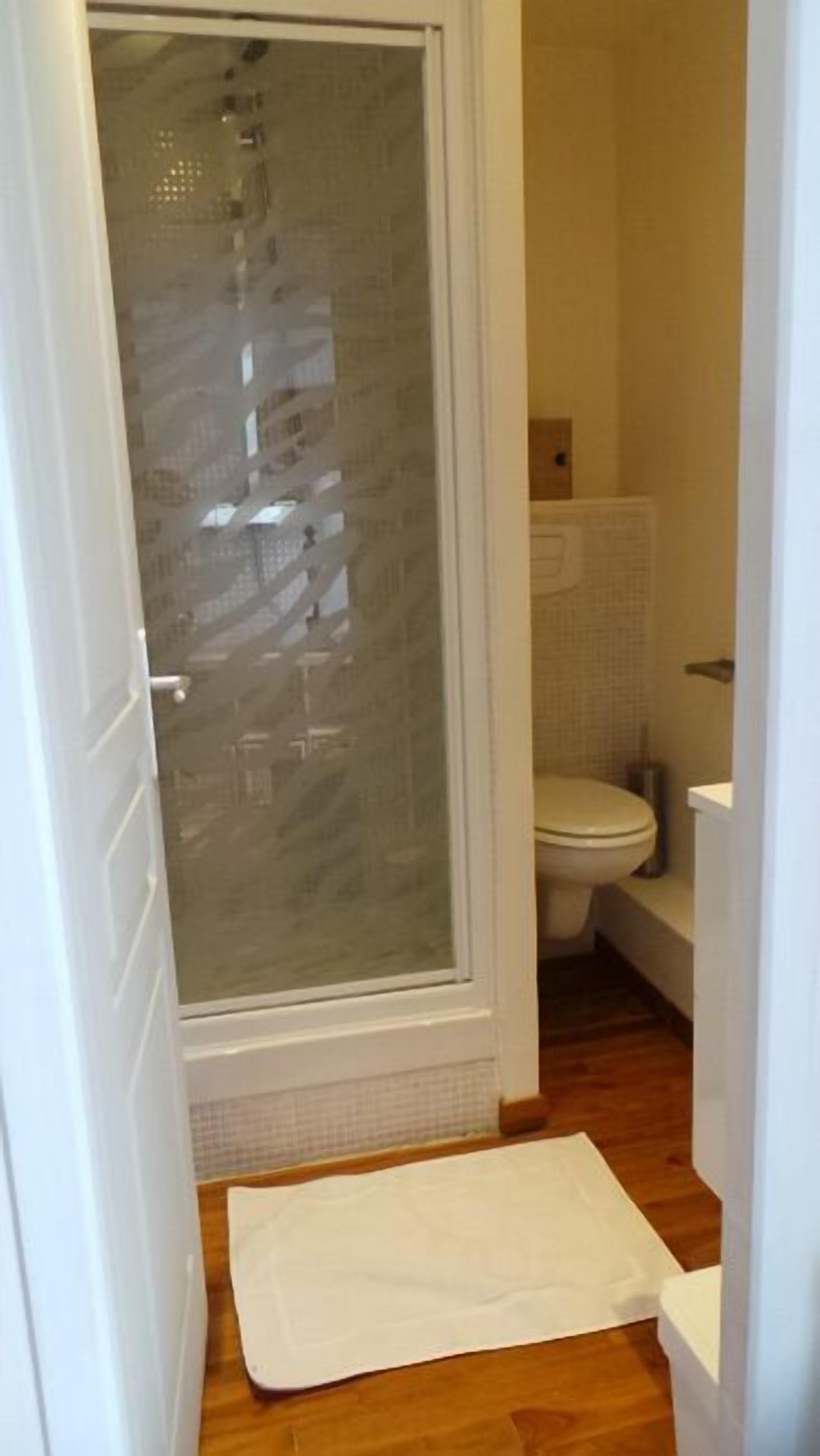 Un baño con cabina de ducha de vidrio, inodoro y suelo de madera.
