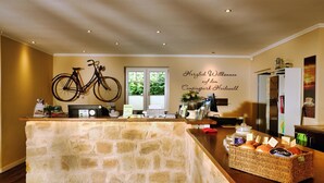 A reception area with a stone counter, a bicycle mounted on the wall, a coffee station, and a welcome sign. - Campingpark Heidewald (Sassenberg)