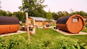 A row of wooden barrel-shaped cabins with a grassy yard and a hammock. - Campingpark Heidewald (Sassenberg)