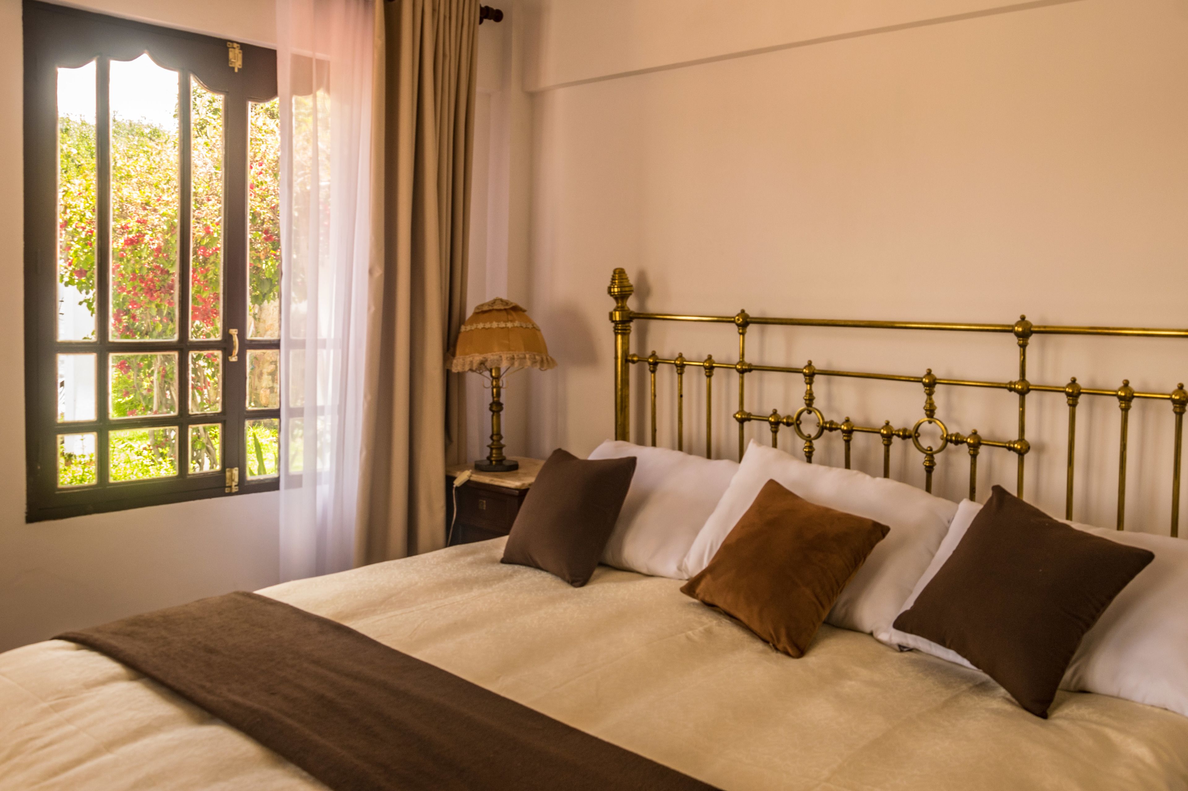 A bedroom with a bed, a window with curtains, and a bedside table with a lamp.