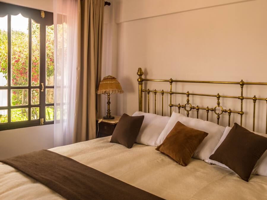 A bedroom with a bed, a window with curtains, and a bedside table with a lamp.