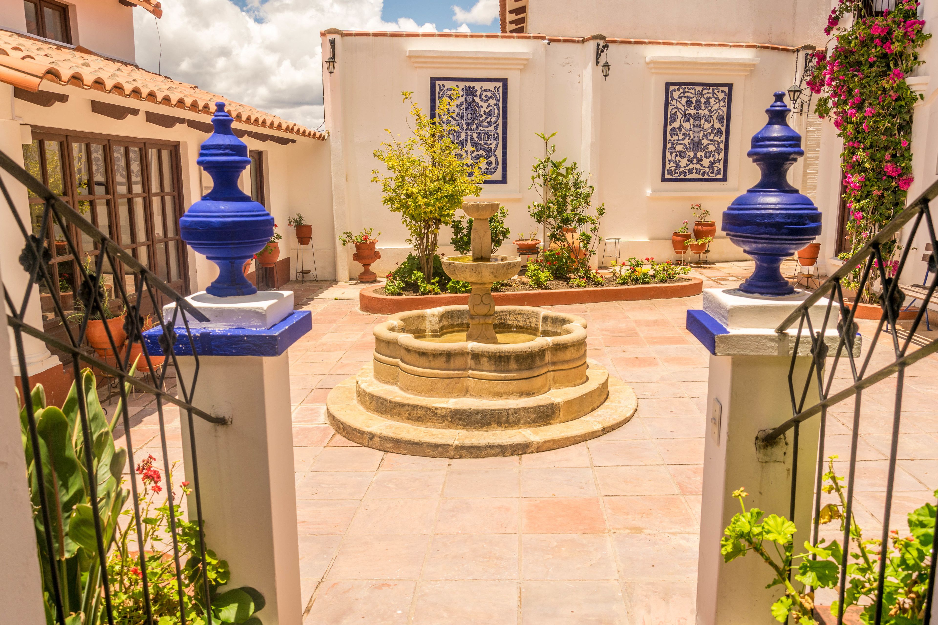 Un patio con una fuente, plantas en macetas y jarrones azules decorativos.