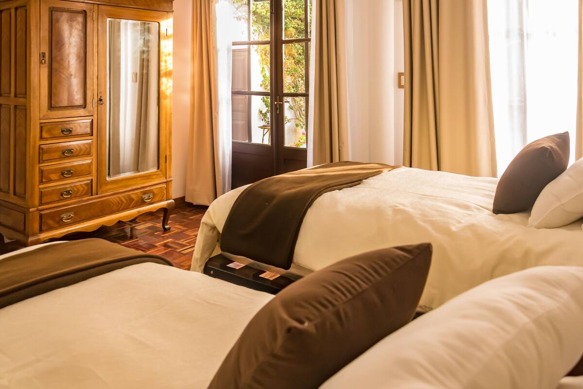 A hotel room with two beds, a wooden dresser, and a window with curtains.