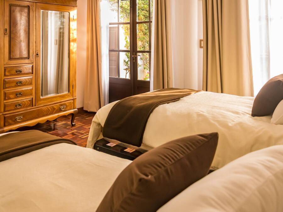 Una habitación de hotel con dos camas, un aparador de madera y una ventana con cortinas.