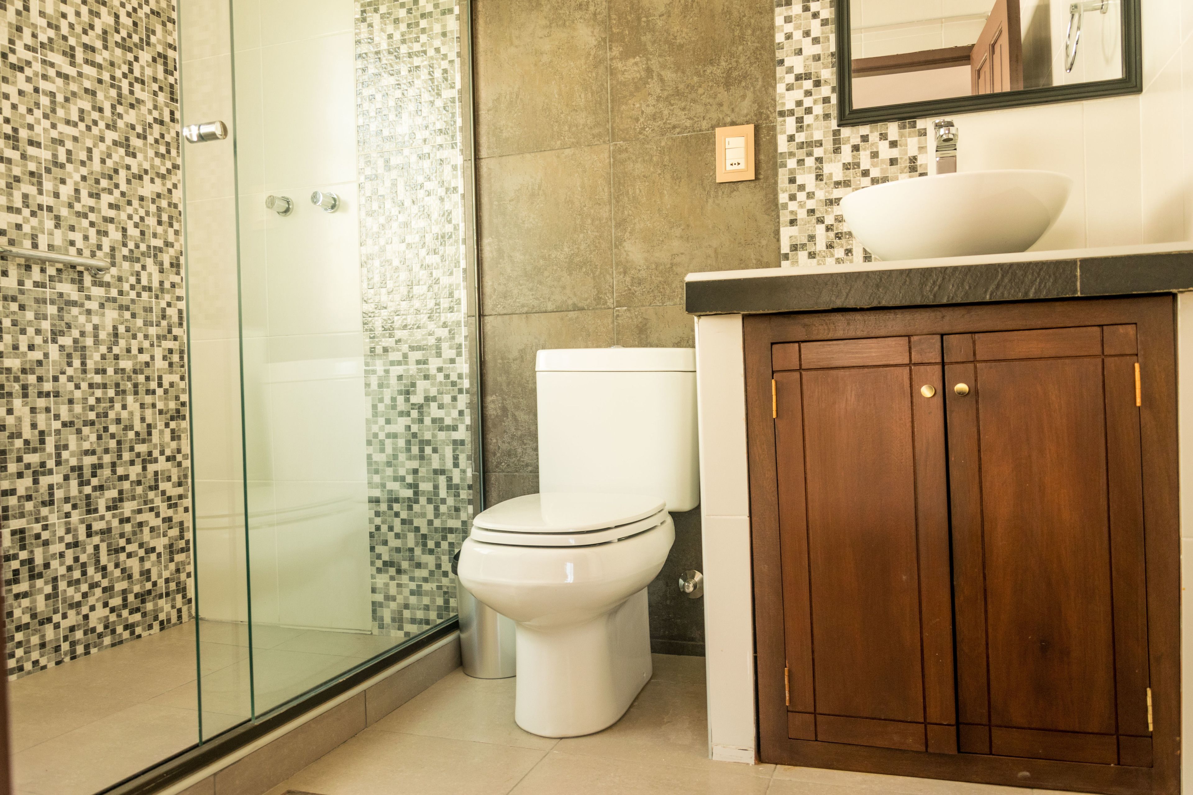 Une salle de bain avec une douche à parois de verre, des toilettes blanches et un meuble-lavabo en bois avec un évier.
