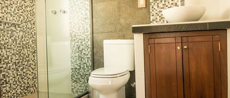Une salle de bain avec une douche à parois de verre, des toilettes blanches et un meuble-lavabo en bois avec un évier.
