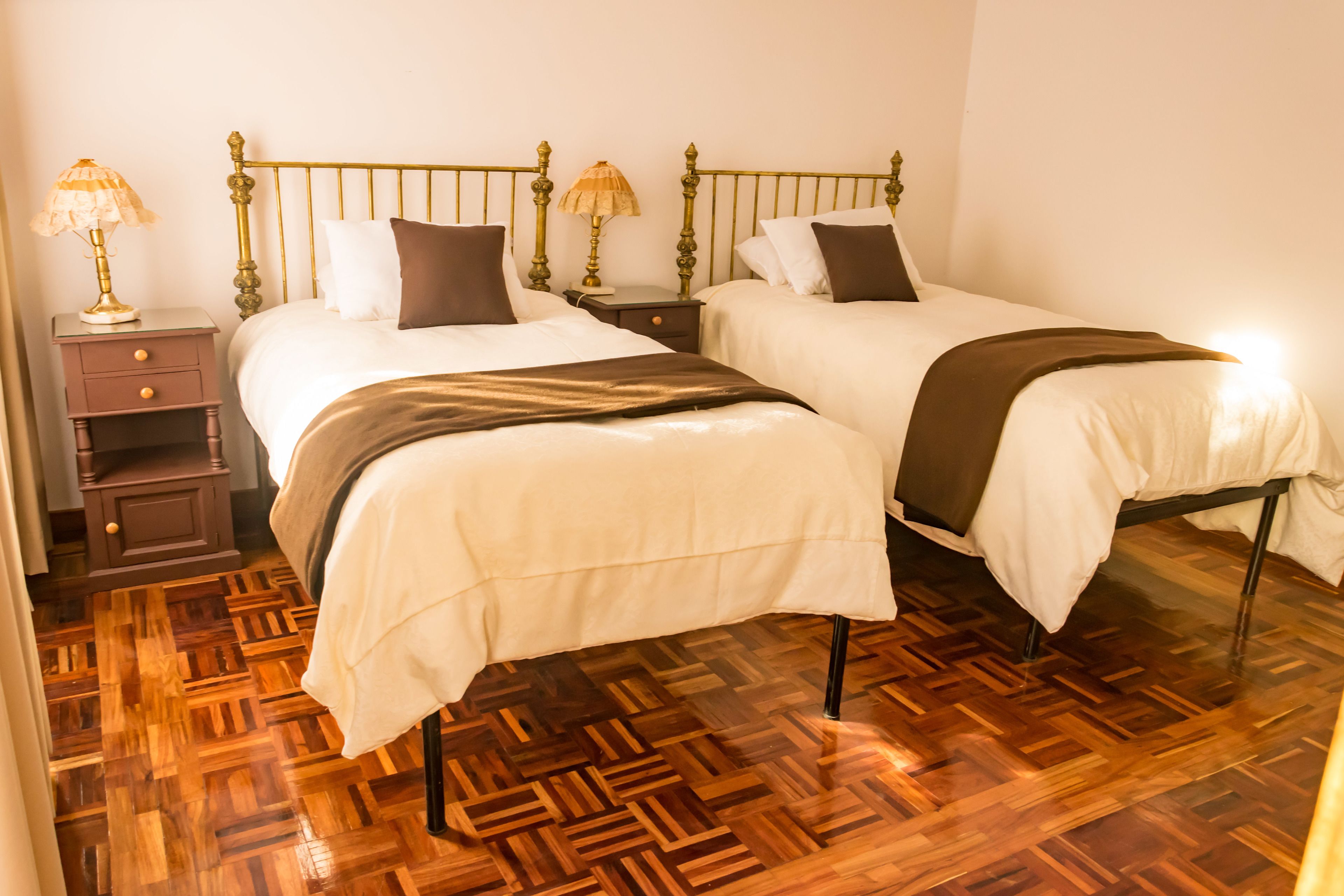 A hotel room with two beds, a nightstand, and a lamp.