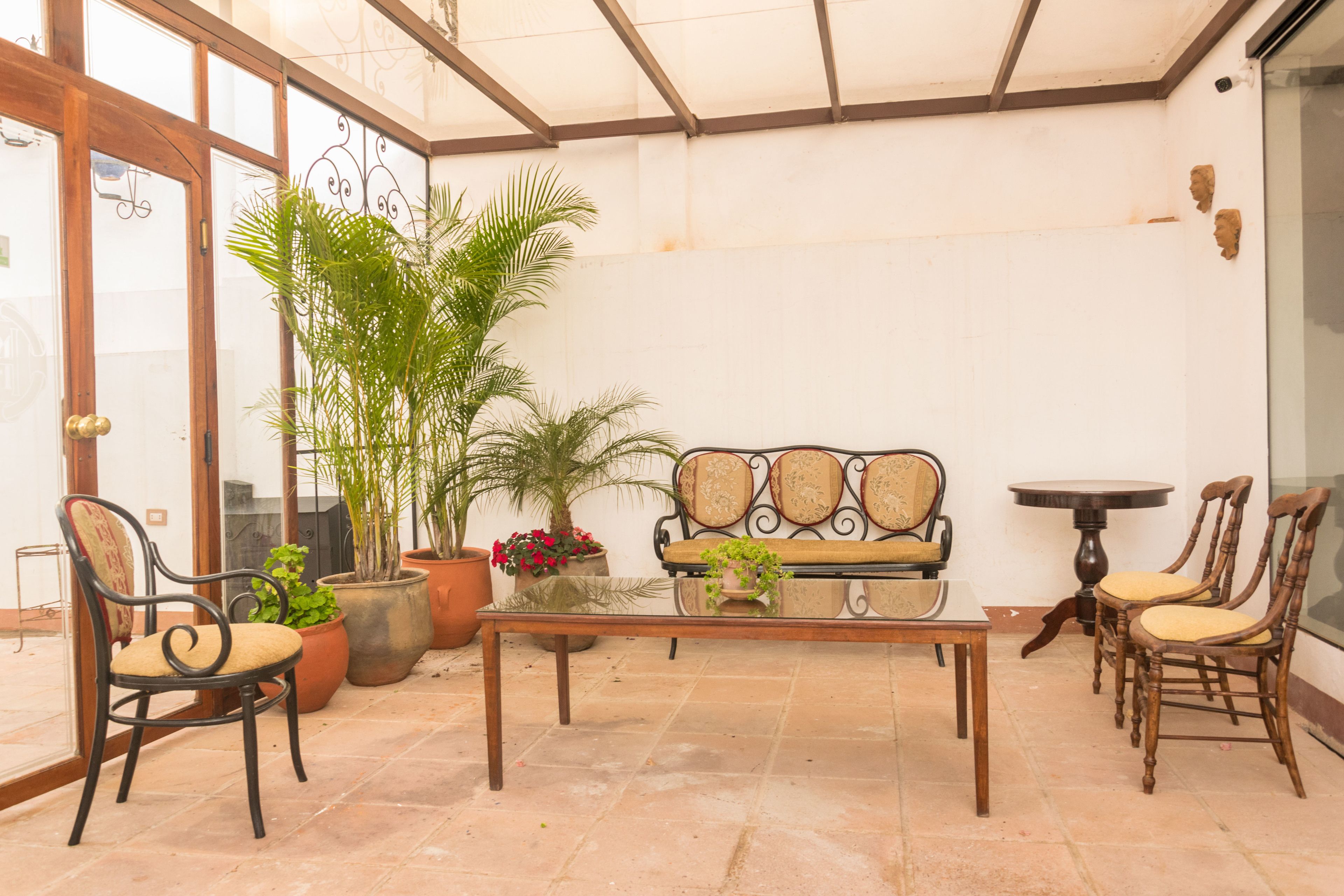 A sunlit patio with a wooden table, cushioned chairs, a sofa, and potted plants.