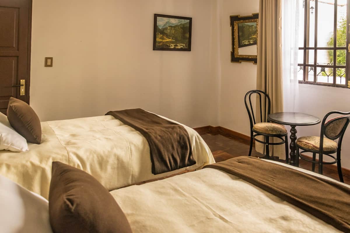 A hotel room with two beds, a small table with chairs, and a window with curtains.