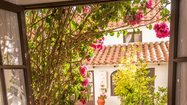 An indoor patio with two wooden chairs and a small table, surrounded by a garden with flowering plants and a tiled floor. - El Jardin De Su Merced B&B (Sucre)